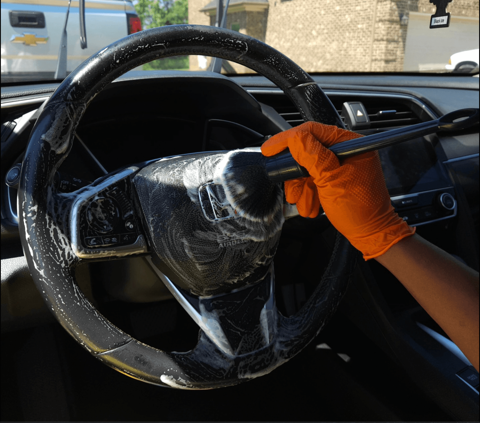 Detailer in nitrile gloves wiping down a foamy steering wheel during an interior deep clean